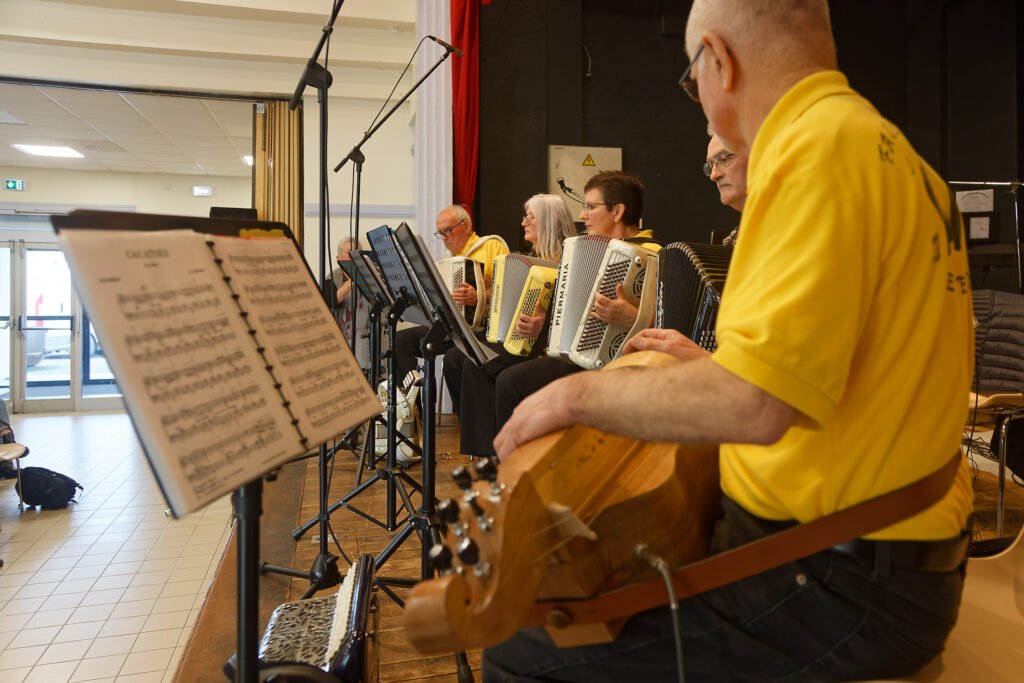 L’orchestre Fa Si l’Accordéon en pleine performance sur la scène de la salle Clemenceau à La Réorthe, avec 11 accordéonistes, deux trompettistes et trois chanteuses.